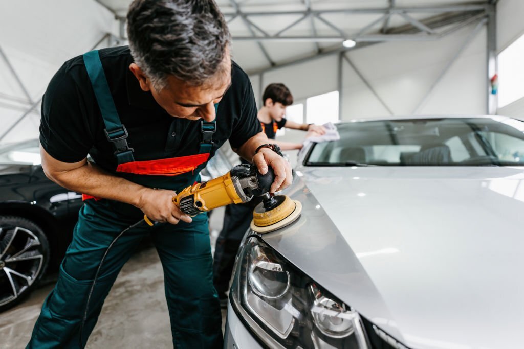 Car detailing - Hands with orbital polisher in auto repair shop. Selective focus.