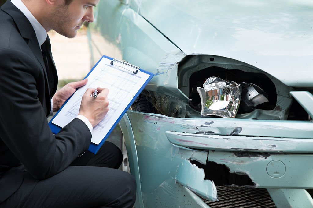 Side view of writing on clipboard while insurance agent examining car after accident