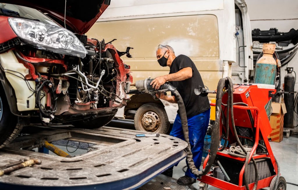 Mechanic holding a spot welding machine for welding front car part at auto garage